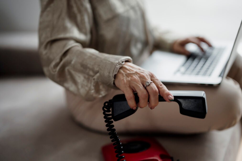 Person holding a telephone receiver while working on a laptop
